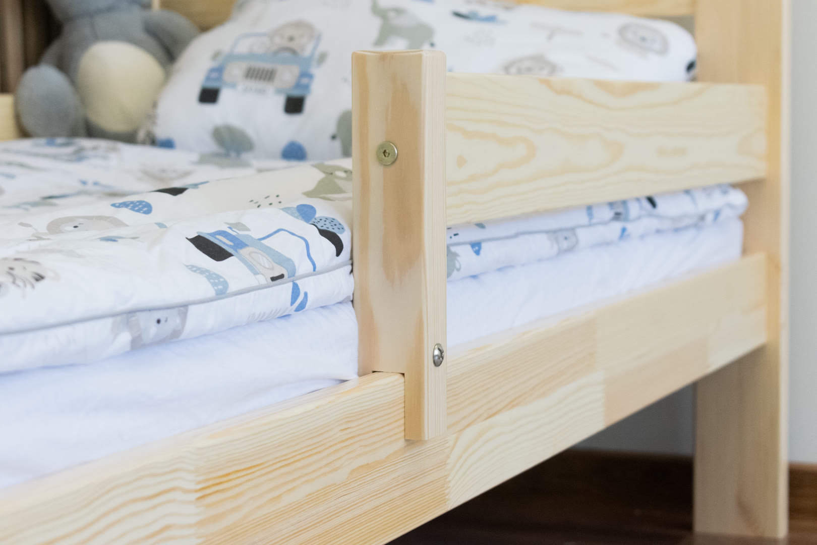 Łóżko dziecięce z drewna sosnowego ustawione przy ścianie nad miękkim dywanem w pokoju przedszkolaka